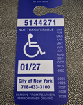 Handicap parking permit tag with serial number and expiration date on a textured surface NY